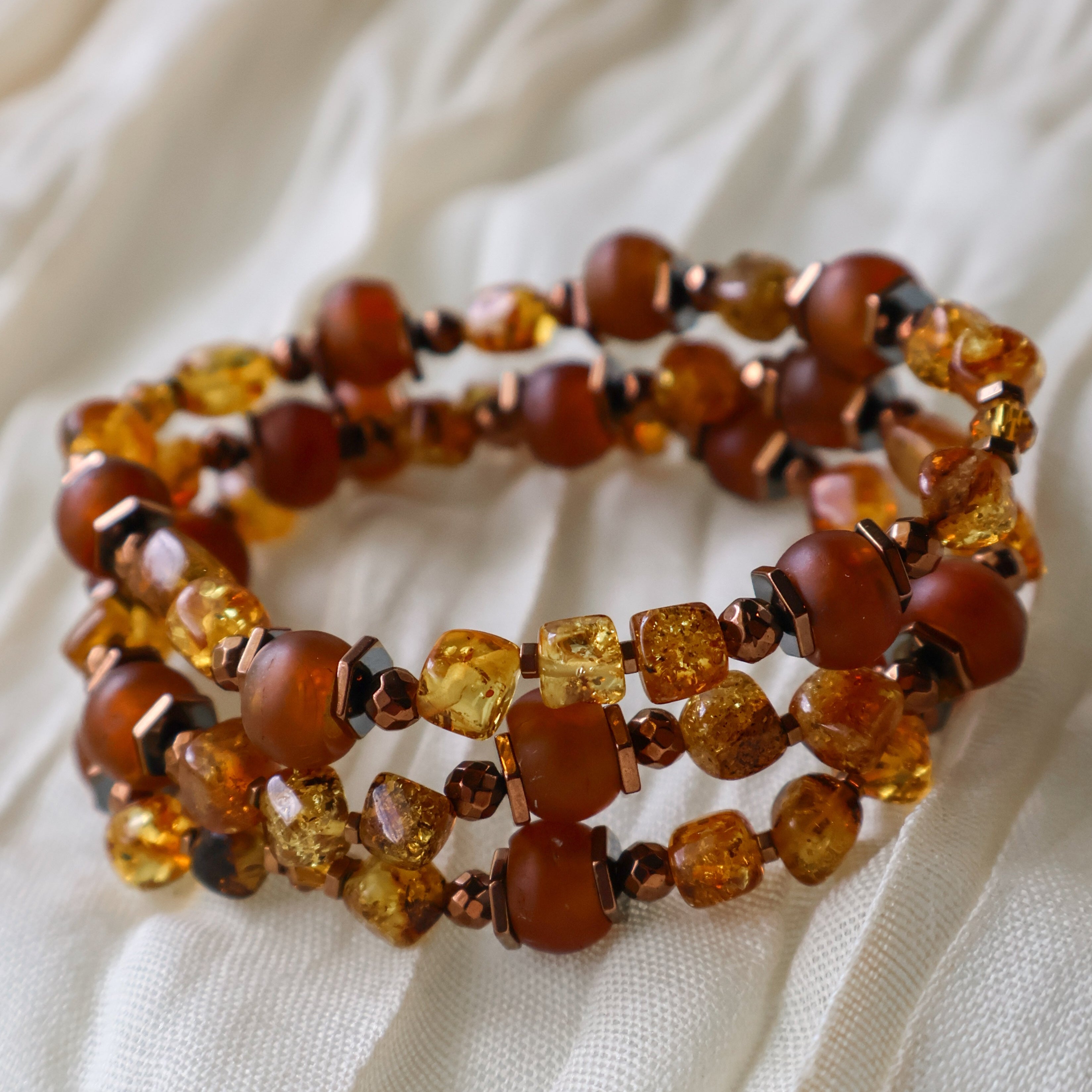 Stack of amber beaded bracelets on a beige fabric background