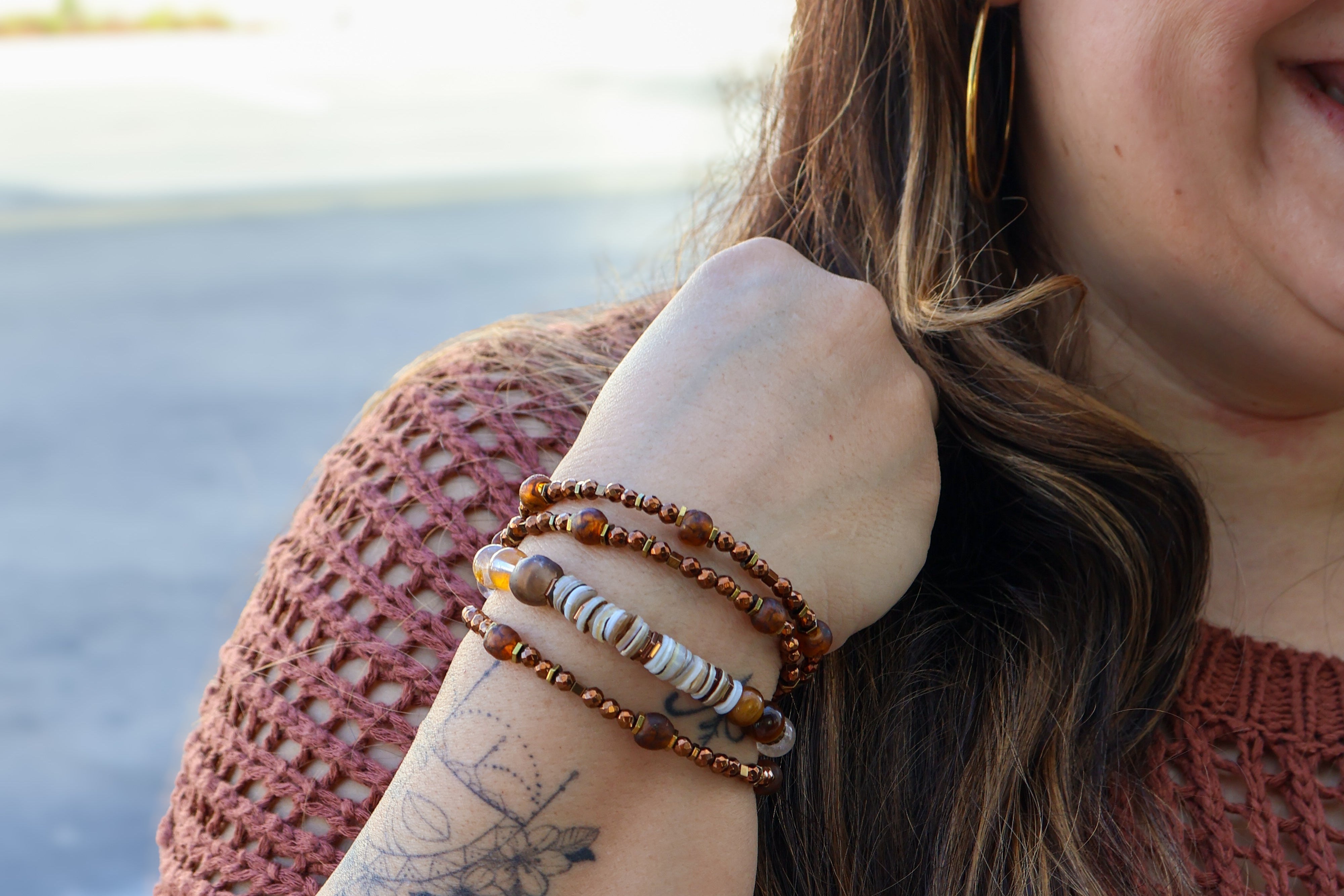 Woman with tattoos on her arm wearing multiple bracelets, outdoors.