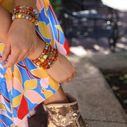 Person wearing colorful floral dress and gold sequin boots with bracelets on a blurred outdoor background