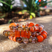 Stack of orange and brown beaded bracelets on a textured surface with blurred greenery in the background