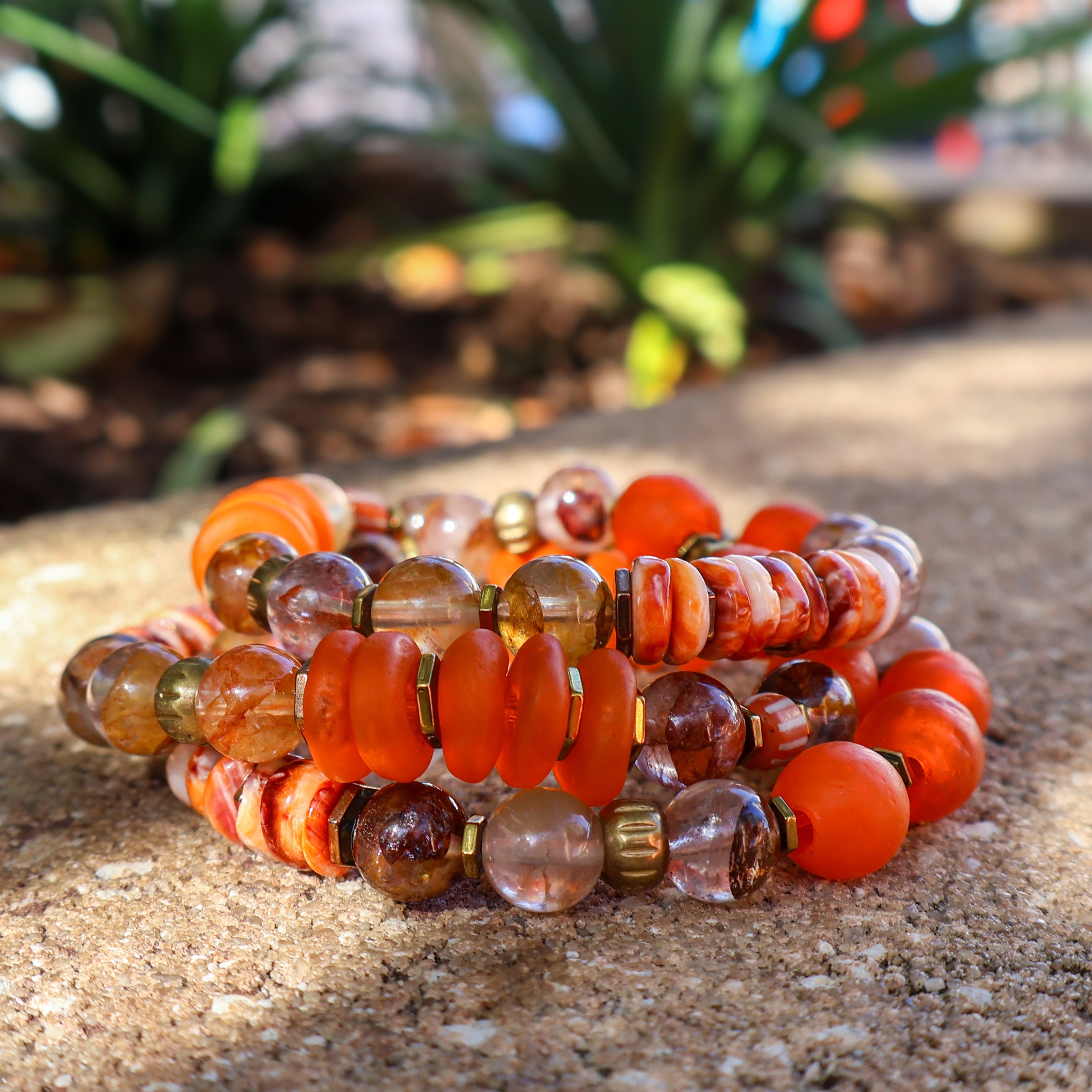 Stack of orange and brown beaded bracelets on a textured surface with blurred greenery in the background