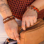 Person zipping a brown leather bag with tattoos and bracelets visible